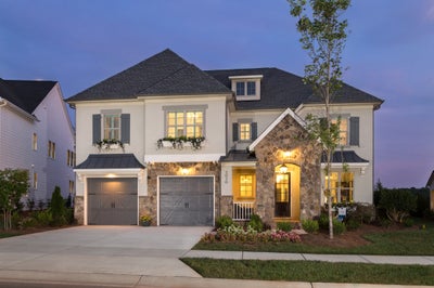 Two-story home with white stucco, stone accents, dark roof, and two-car garage at twilight