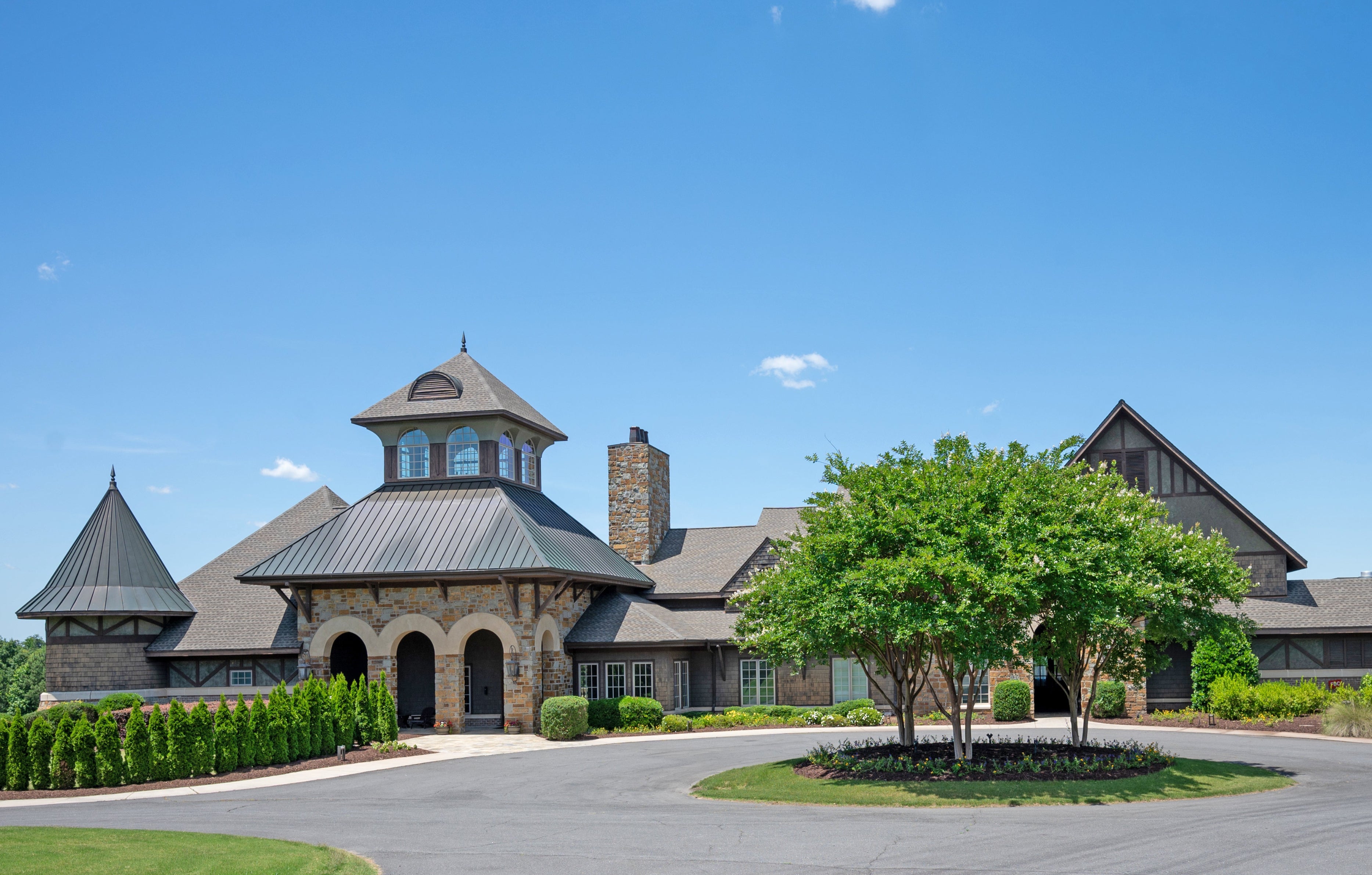 Large estate home with stone facade, cupola, and circular driveway with landscaped center island
