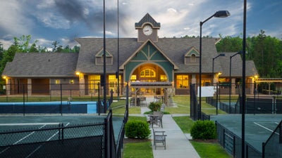 Community clubhouse with clock tower and outdoor tennis courts at dusk