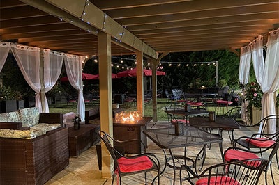 Covered outdoor patio with dining tables, string lights, white curtains, and fire feature