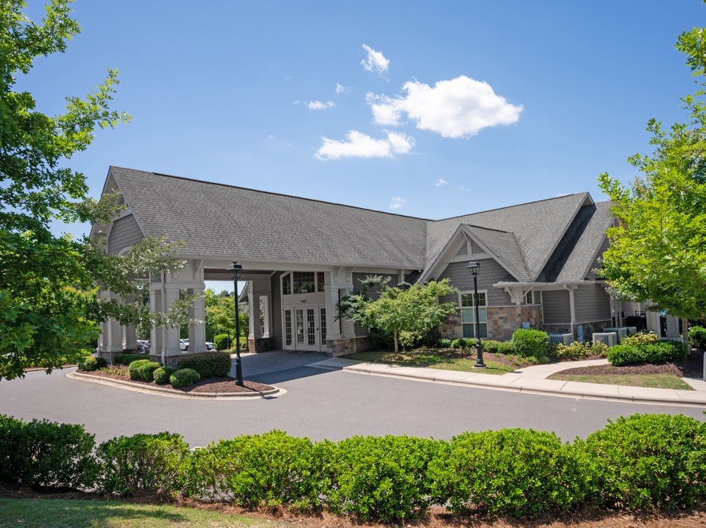 Community clubhouse with covered entrance and gray siding surrounded by landscaping