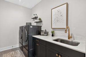 Laundry room with dark gray cabinets, white countertop, undermount sink, and gold faucet