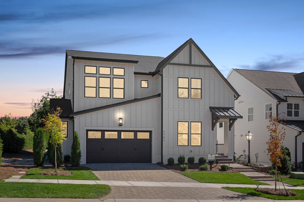 Two-story modern farmhouse with gray siding, black trim, and two-car garage at dusk