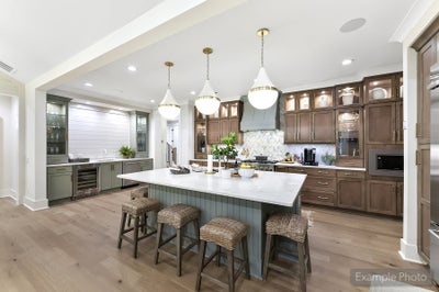 Open kitchen with brown cabinets, white island with wicker stools, and three pendant lights