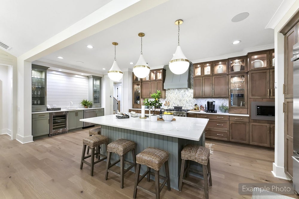 Open kitchen with brown cabinets, white island with wicker stools, and three pendant lights