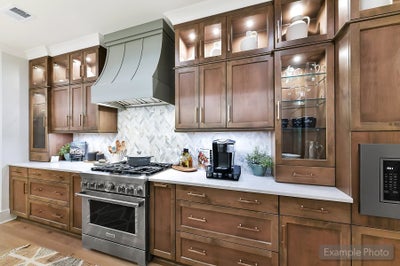Kitchen with brown wood cabinets, white countertops, stainless steel range, and decorative hood
