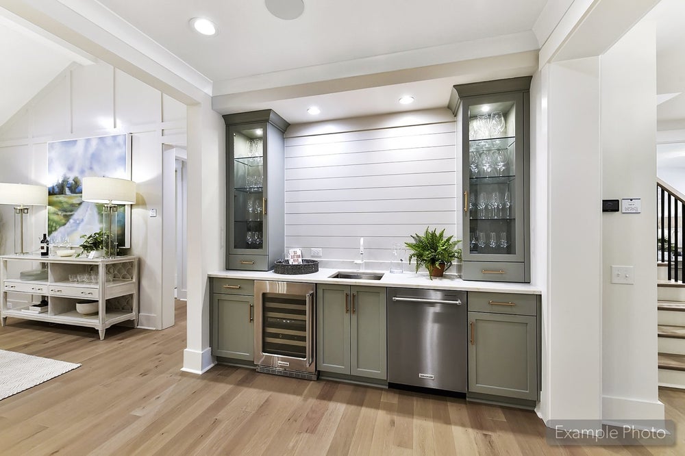 Wet bar with gray-green cabinets, glass display cases, wine cooler, and shiplap accent wall