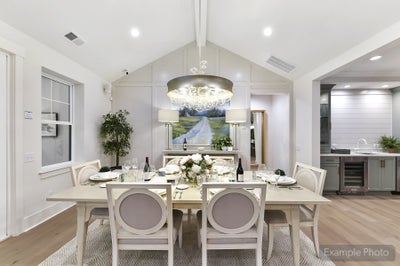 Open-concept dining room with vaulted ceiling, white table, and modern chandelier adjacent to kitchen
