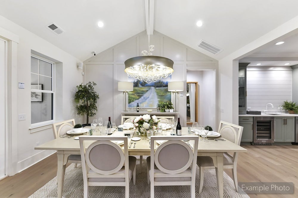 Open-concept dining room with vaulted ceiling, white table, and modern chandelier adjacent to kitchen
