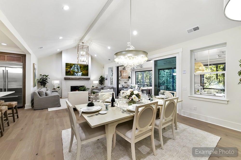 Open-concept living and dining area with vaulted ceilings, white furniture, and hardwood floors