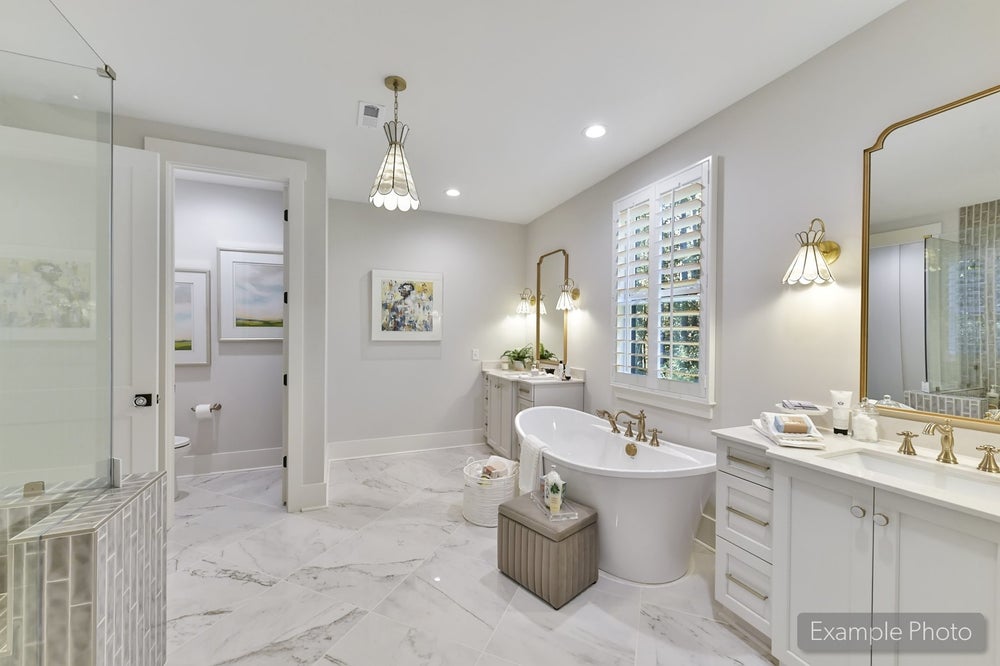 Spacious master bathroom with freestanding tub, marble floors, white vanity, and gold fixtures
