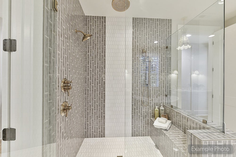 Walk-in shower with gray vertical tile, glass enclosure, and gold fixtures