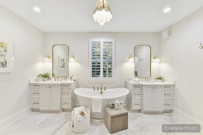 Master bathroom with freestanding tub, dual vanities, gold mirrors, and marble flooring