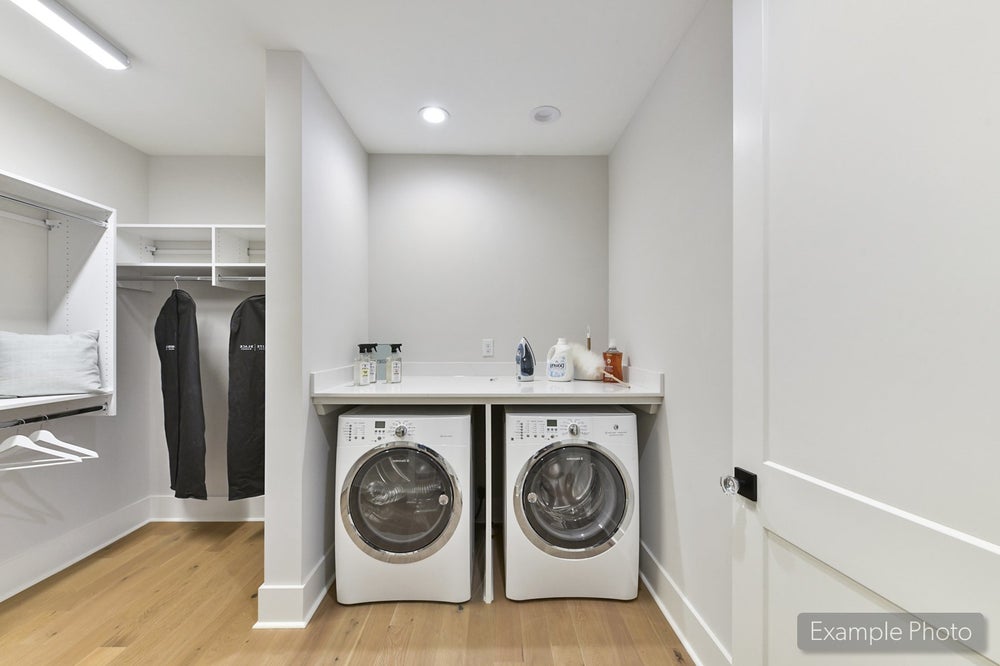 Laundry room with front-load washer and dryer, white shelving, and wood floors