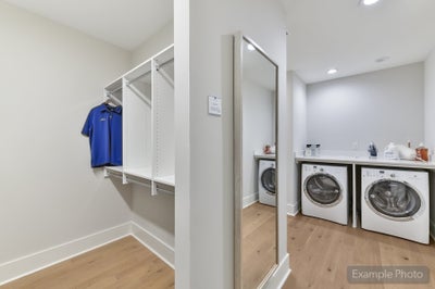 Laundry room with white front-load washer and dryer, built-in shelving, and wood floors
