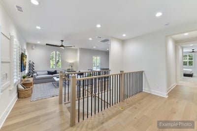 Upper floor landing with modern metal railing, light wood floors, and open living area with ceiling fan