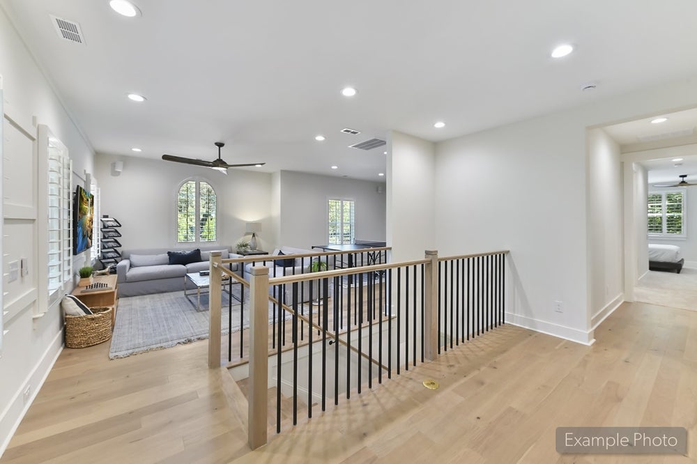 Upper floor landing with modern metal railing, light wood floors, and open living area with ceiling fan