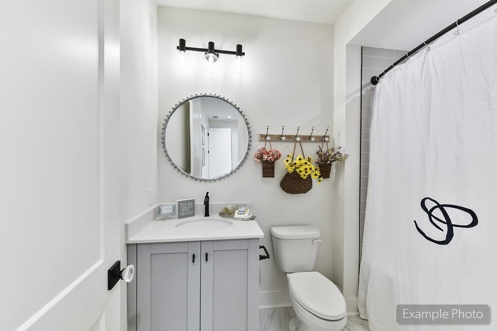 Bathroom with gray vanity, round mirror, white shower curtain, and decorative wall hooks