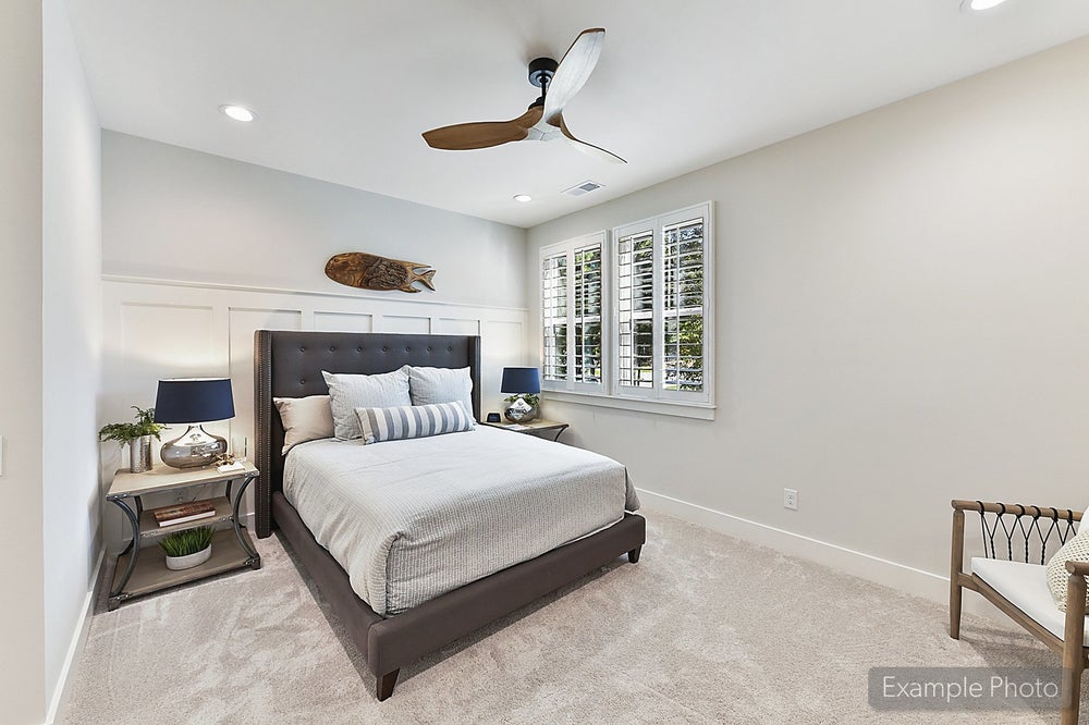 Bedroom with dark upholstered bed, white plantation shutters, ceiling fan, and beige carpet