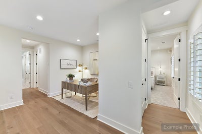 Home office with wooden desk and white walls leading to hallway with hardwood floors