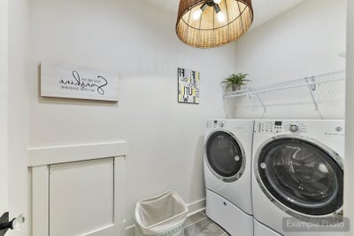 Laundry room with white front-load washer and dryer, wall shelf, and wicker pendant light