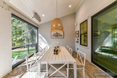 Screened porch with dining table, white chairs, and wicker pendant light