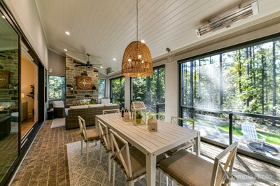 Screened porch with dining table, wicker pendant light, and floor-to-ceiling windows overlooking wooded yard