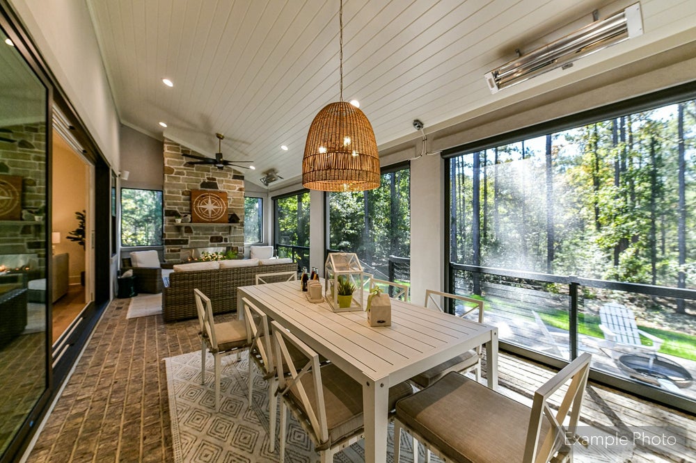 Screened porch with dining table, wicker pendant light, and floor-to-ceiling windows overlooking wooded yard