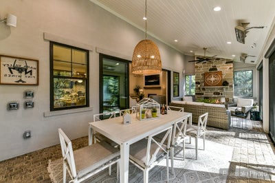 Covered outdoor patio with dining table, wicker furniture, brick fireplace, and pendant lighting