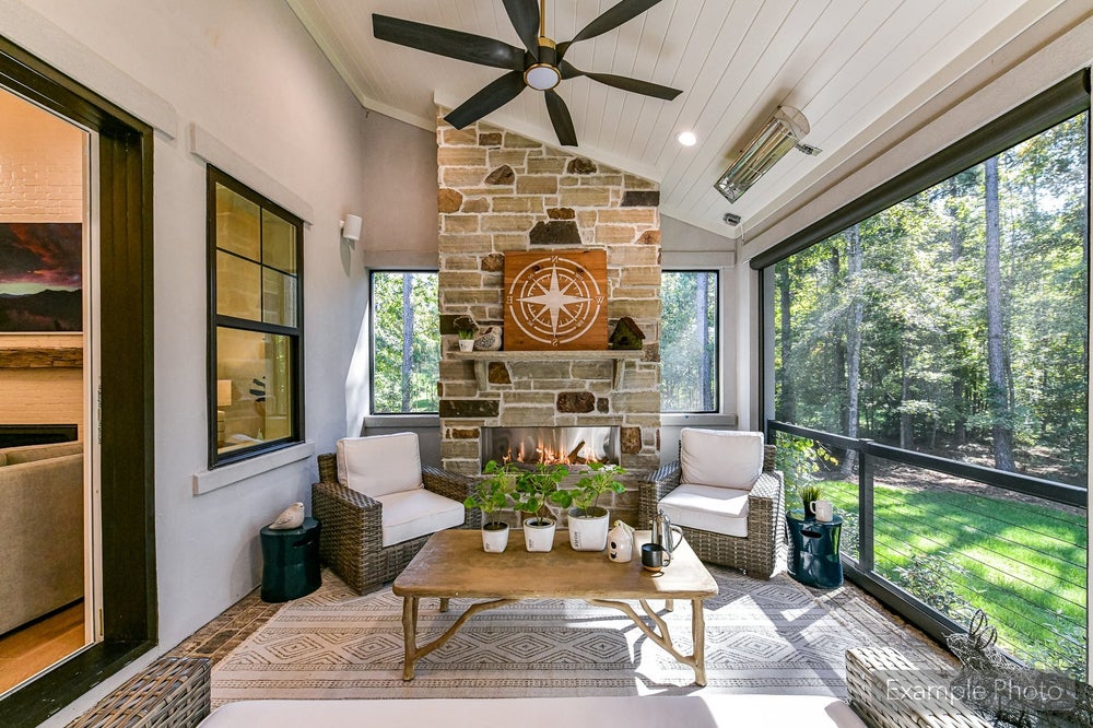 Screened porch with stone fireplace, vaulted ceiling, and wicker furniture overlooking wooded yard