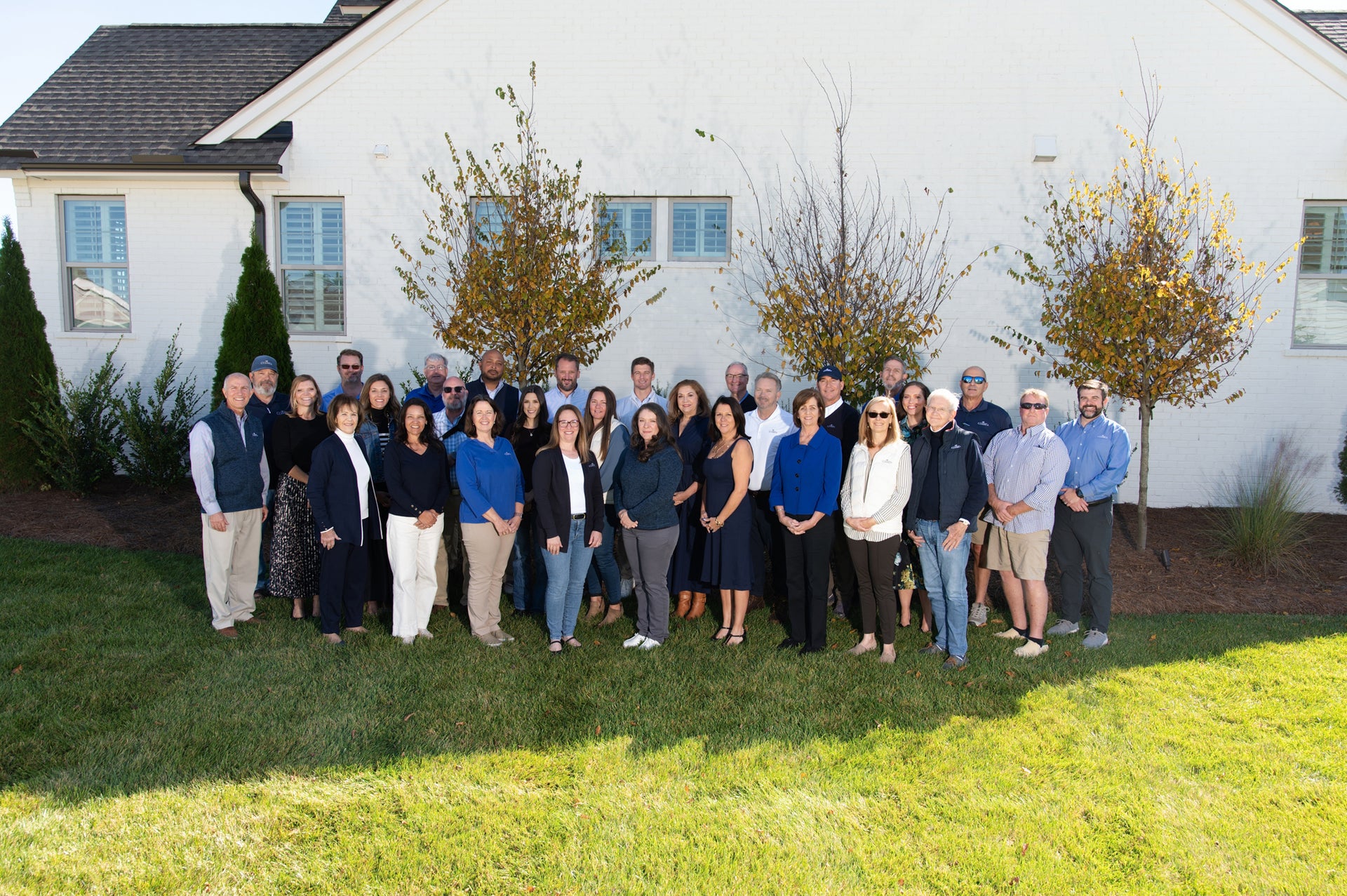 Large group of real estate professionals standing in front of white stucco home with dark roof