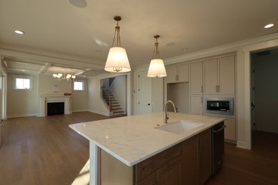 Modern kitchen with large white marble island, pendant lights, and gray cabinets in open floor plan.