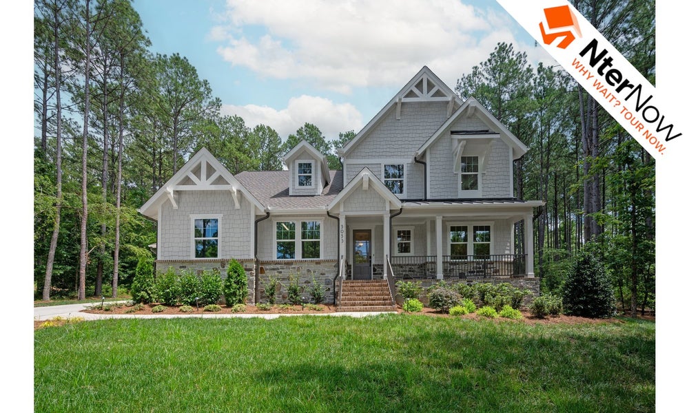 Large two-story house with gray siding, white trim, and covered front porch surrounded by trees.