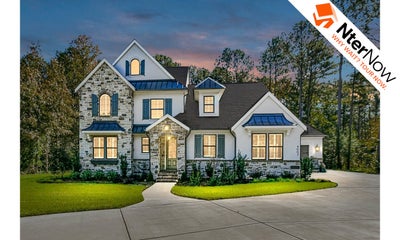Large two-story house with stone and white exterior, lit windows, and green lawn at dusk.