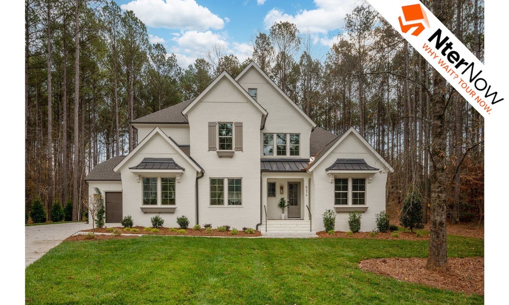 Large white two-story house with multiple gabled roofs and front steps surrounded by trees.
