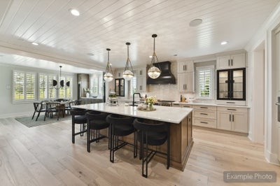 Open kitchen with large island, black barstools, pendant lights, white cabinets, and shiplap ceiling open to dining area