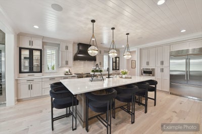 Large kitchen with white cabinets, center island with black barstools, pendant lights, and stainless steel appliances