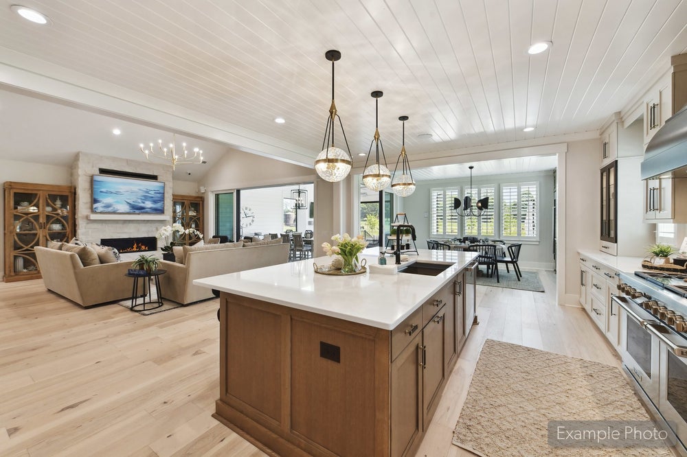 Open-concept kitchen with large wood island, white countertops, and pendant lights, flowing into living and dining areas with hardwood floors