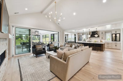 Open-concept living room with vaulted ceiling, hardwood floors, and kitchen visible in background