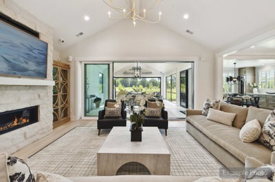 Open living room with vaulted ceiling, stone fireplace, and sliding glass doors to covered patio
