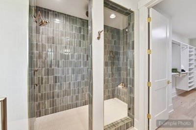 Two walk-in showers with gray tile walls, glass doors, gold fixtures, and a walk-in closet visible nearby.