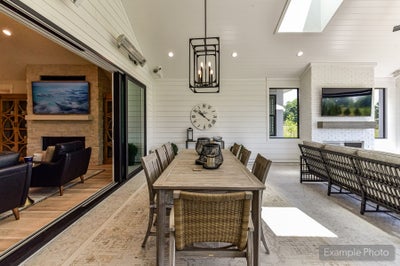 Covered outdoor patio with dining table, pendant light, brick fireplace, and sliding glass doors to living room