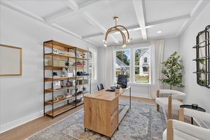 Home office with coffered ceiling, wood desk, open shelving, and large window