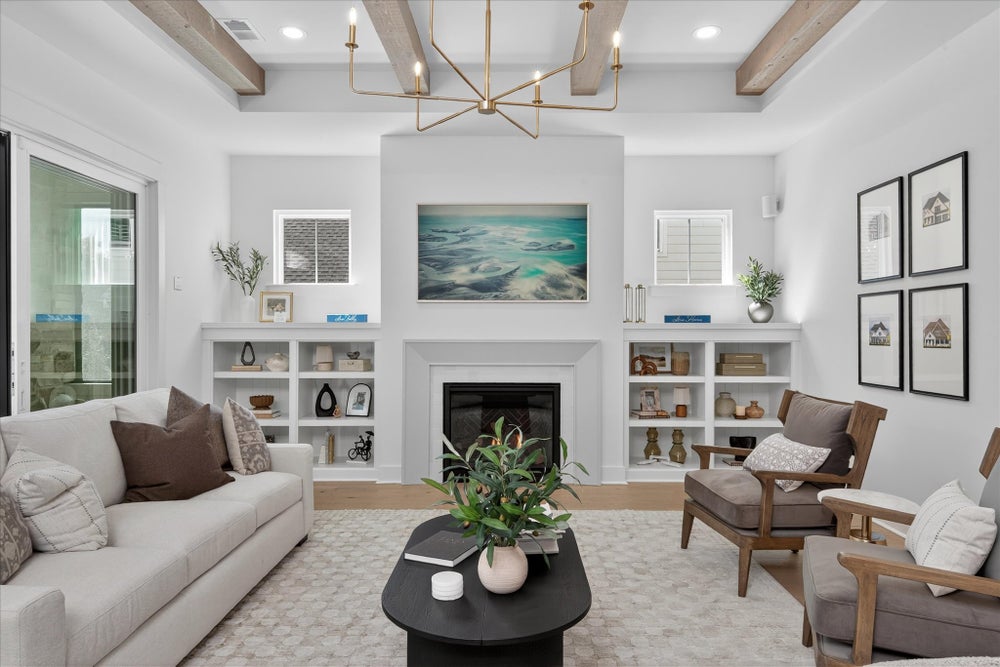 Living room with white fireplace, built-in shelving, exposed wood beams, and modern chandelier