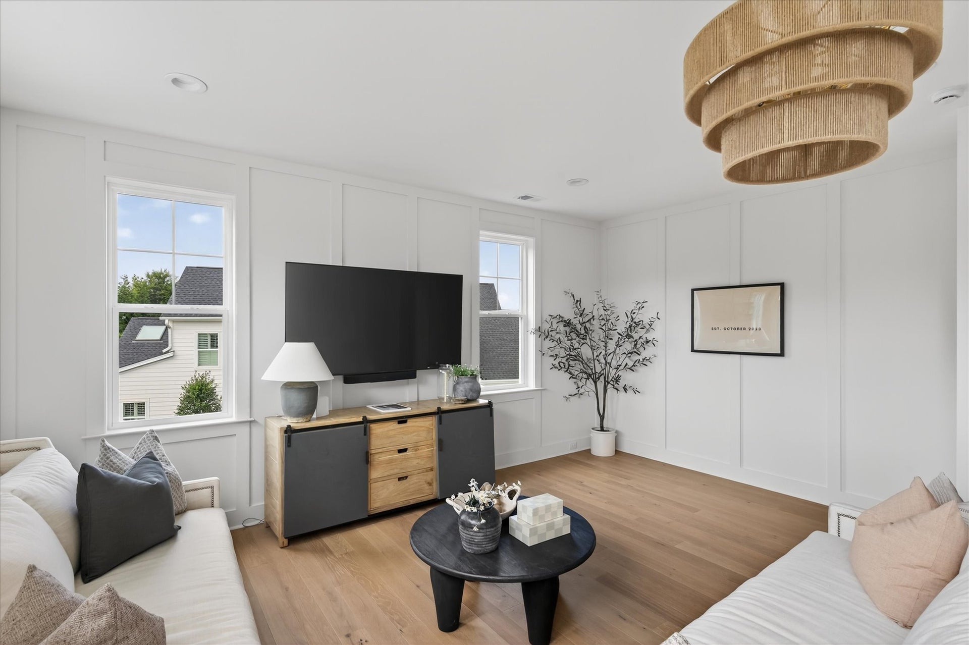 Modern living room with white walls, light wood floors, and tiered woven chandelier