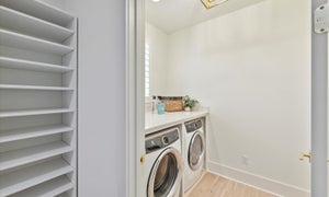Laundry room with front-load washer and dryer, white built-in shelving, and light wood floors