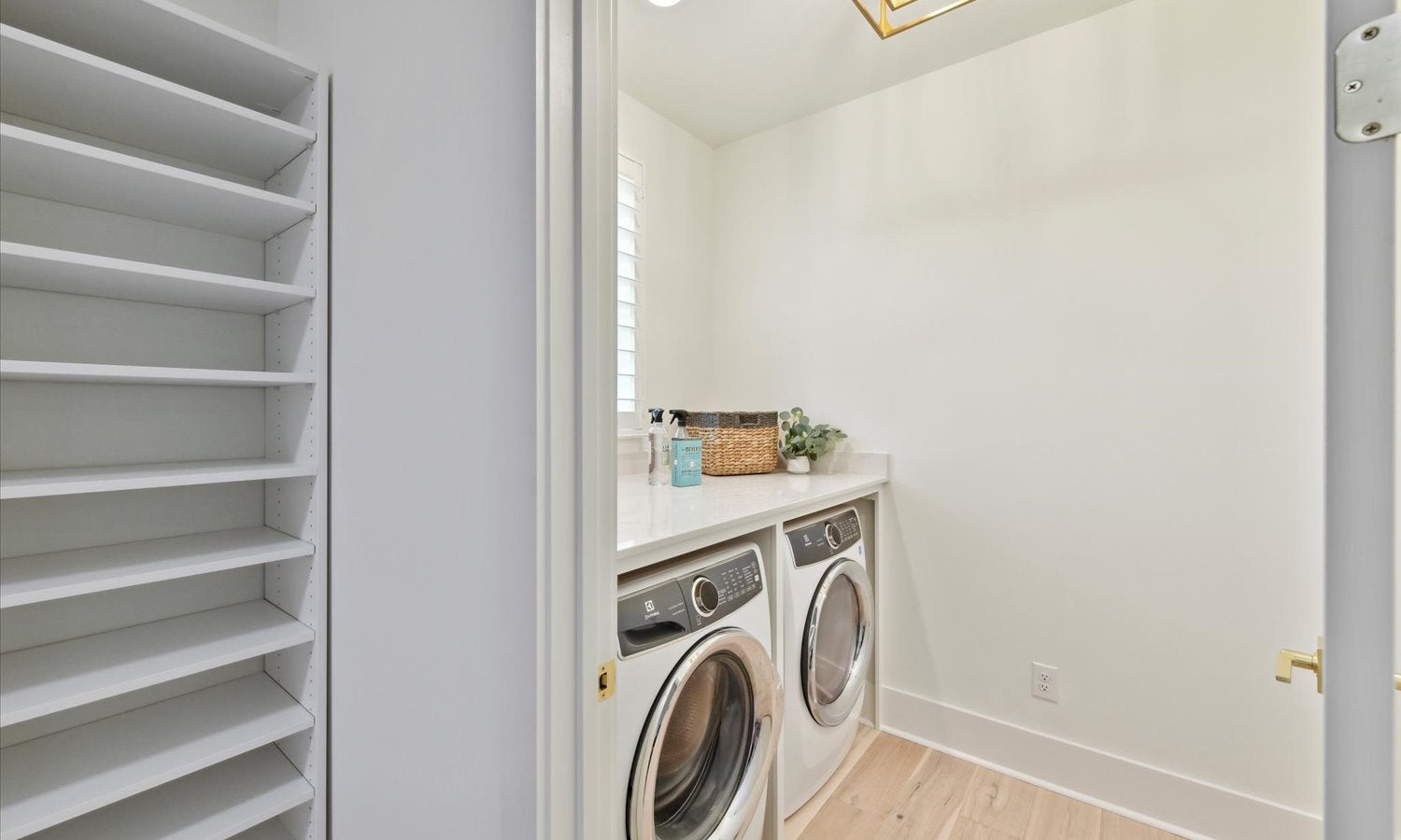 Laundry room with front-load washer and dryer, white built-in shelving, and light wood floors