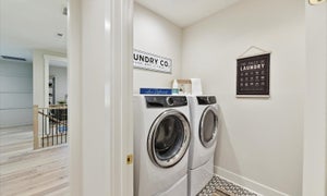 Laundry room with white front-load washer and dryer and decorative wall signs