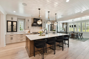 Open-concept kitchen with white cabinets, large island with black stools, and shiplap vaulted ceiling