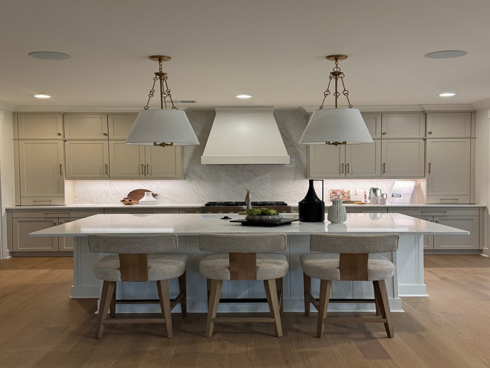 Modern kitchen with beige cabinets, white island, pendant lights, and four bar stools